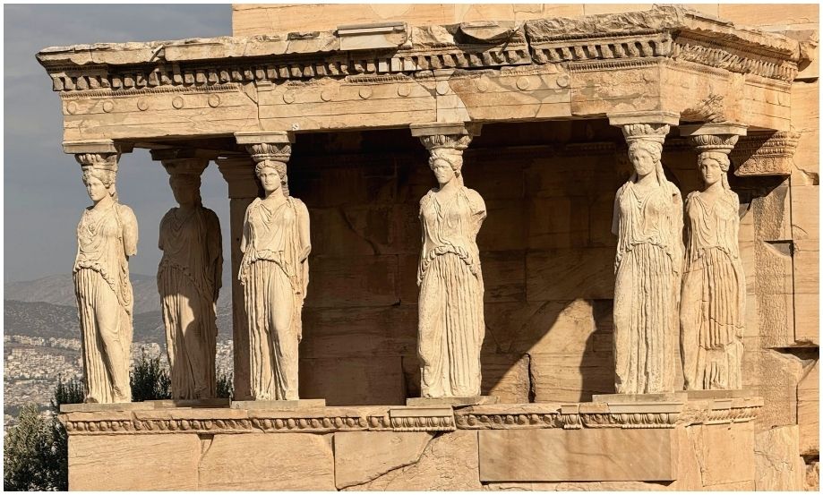 Fotografía detallada del pórtico del Erecteón en la Acrópolis de Atenas, mostrando seis esculturas femeninas de mármol, conocidas como Cariátides, que sostienen la estructura bajo la cálida luz del sol.