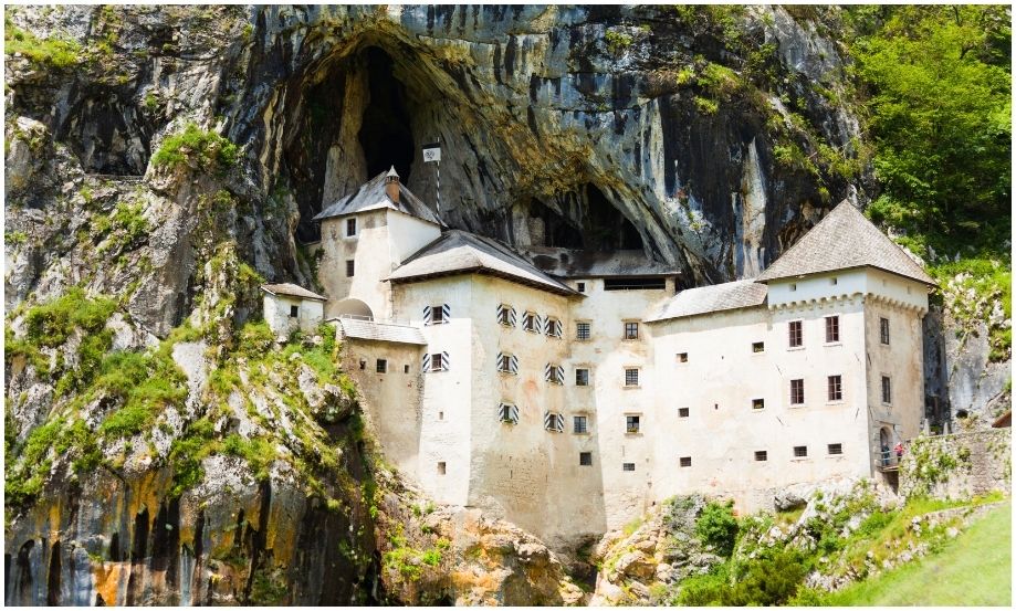 Vista exterior del majestuoso Castillo de Predjama incrustado en la boca de una enorme cueva cárstica en Eslovenia, mostrando su fachada blanca contrastando con la roca oscura.