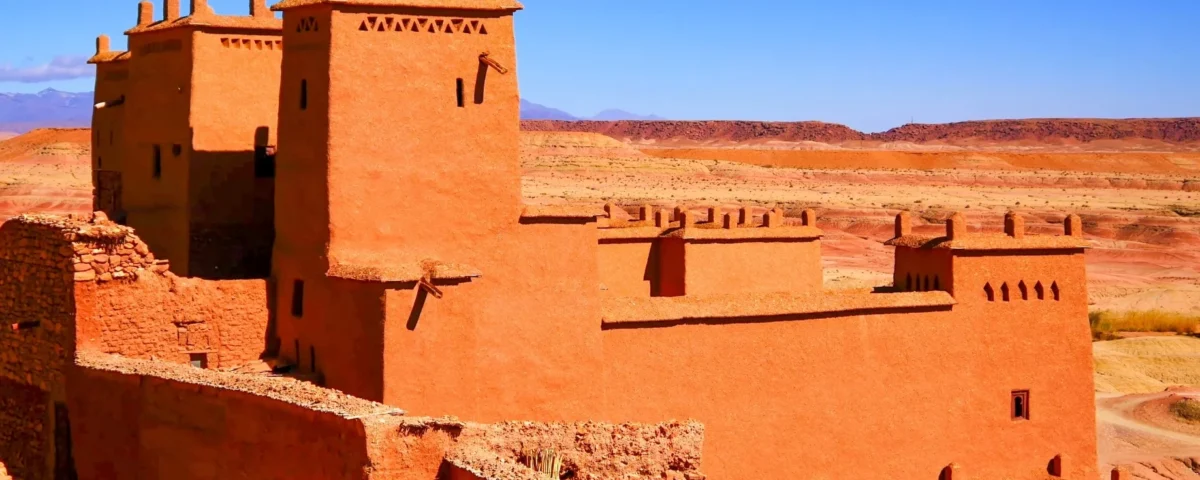 Fachada de arcilla roja del Ksar de Aït Benhaddou con el horizonte árido del valle de Ounila de fondo, capturando la textura rugosa de la construcción tradicional.