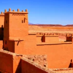 Fachada de arcilla roja del Ksar de Aït Benhaddou con el horizonte árido del valle de Ounila de fondo, capturando la textura rugosa de la construcción tradicional.
