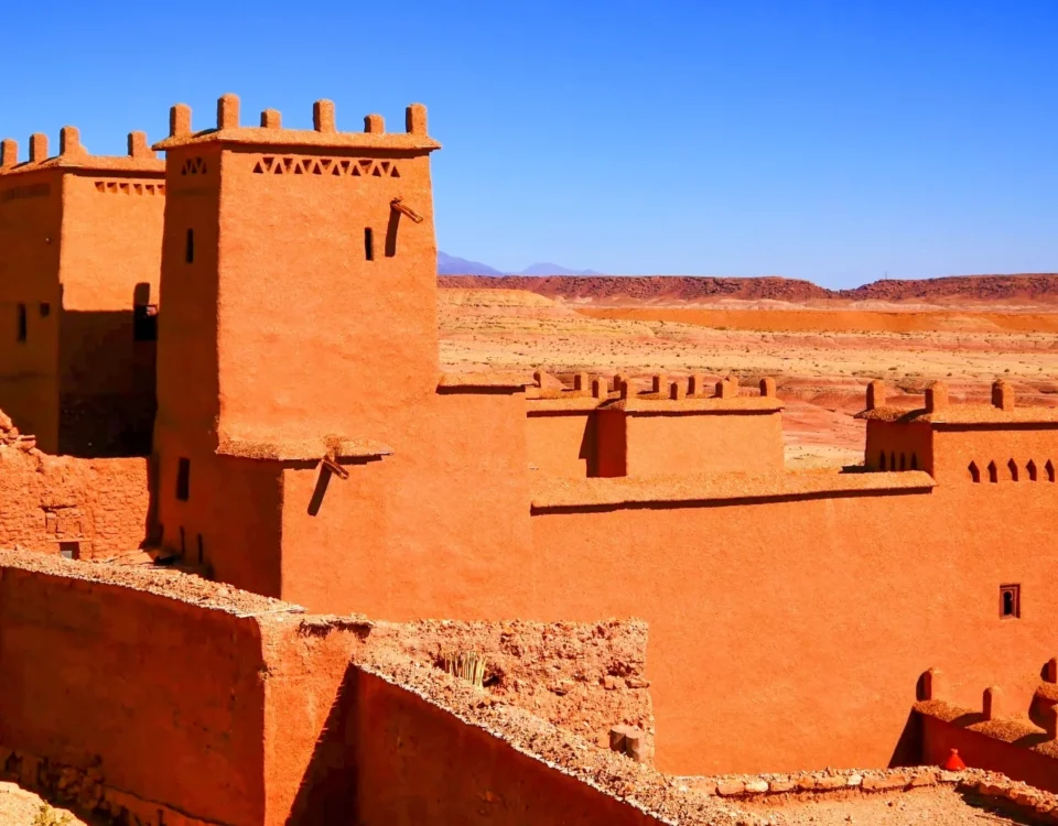Fachada de arcilla roja del Ksar de Aït Benhaddou con el horizonte árido del valle de Ounila de fondo, capturando la textura rugosa de la construcción tradicional.