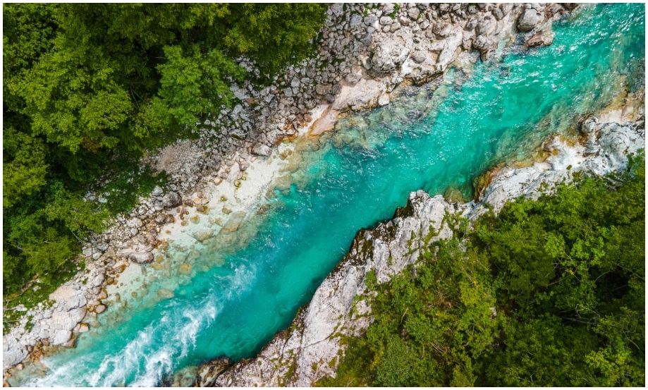 Vista aérea de dron del río Soča de color turquesa intenso en Eslovenia, fluyendo a través de un estrecho cañón de roca caliza pálida, con densos bosques verdes a ambos lados.