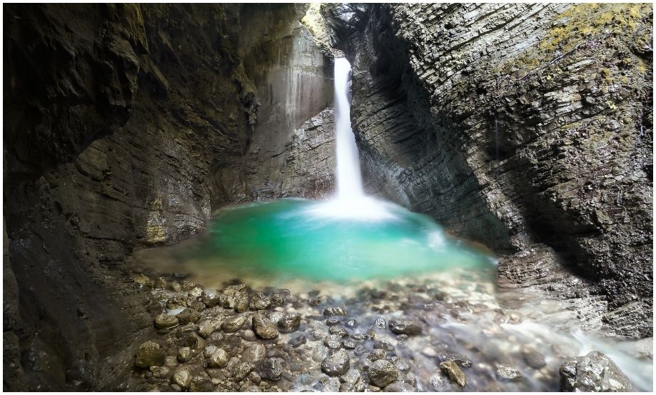 Larga exposición de la cascada oculta Slap Kozjak en Kobarid, mostrando el fuerte contraste entre las paredes de piedra oscura y el agua turquesa iluminada.