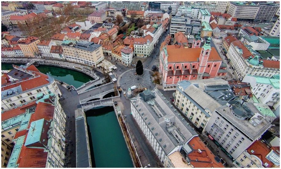 Fotografía aérea del centro histórico de Ljubljana mostrando el icónico Triple Puente de piedra blanca cruzando las aguas verde esmeralda del río, conectando directamente con la Plaza Prešeren.